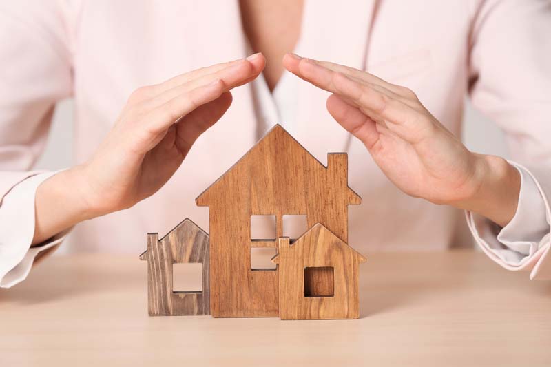 Female agent covering wooden houses at table, closeup. Home insu